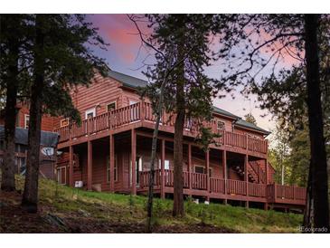 Stunning multi-level home with wood siding and multiple decks, surrounded by lush trees and vibrant sunset colors at 11163 Conifer Mountain Rd, Conifer, CO 80433