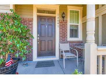 Inviting front entry with brick accents, a cozy chair, and a charming, well-lit porch area at 14641 E Poundstone Dr, Aurora, CO 80015