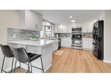 Open kitchen featuring breakfast bar, stainless appliances, gray backsplash and wood flooring at 5050 W 102Nd Ave, Westminster, CO 80031