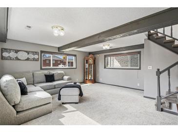 Finished living room features carpet, stairs, wooden beams, and plentiful natural light at 6190 Garrison St, Arvada, CO 80004