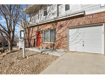 A brick townhouse boasts an attached garage and a vibrant red door adding a pop of color at 5537 Lewis Ct # 101, Arvada, CO 80002