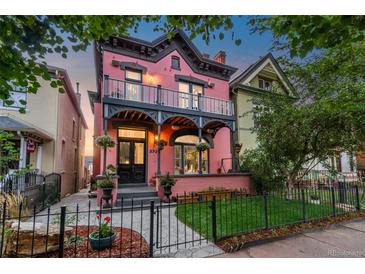 Charming two-story pink home with a lovely wrought iron fenced yard and flowering planters on porch at 2721 Curtis St, Denver, CO 80205