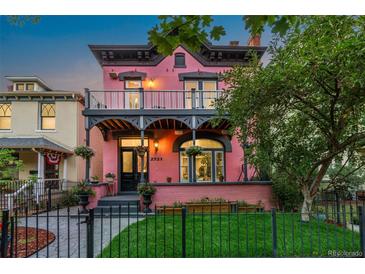 Charming pink Victorian home with a front porch and black iron fence at dusk at 2721 Curtis St, Denver, CO 80205