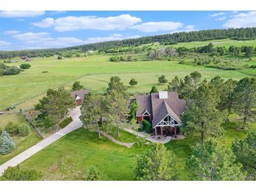 Aerial view of a well-maintained home with mature trees, a long driveway, and surrounded by green fields and forests at 497 Grey Squirrel Way, Franktown, CO 80116
