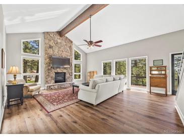 Inviting living room with stone fireplace, vaulted ceilings, wood floors, and bright windows at 30866 Kings Valley Way, Conifer, CO 80433