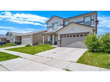 Two-story home with a two-car garage, gray siding and stone accents on the front porch columns at 9923 Truckee St, Commerce City, CO 80022