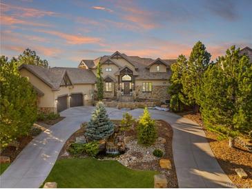 Stately stucco home with stone accents, mature trees, driveway, and landscaping including pond and water feature at 5886 Amber Ridge Dr, Castle Pines, CO 80108