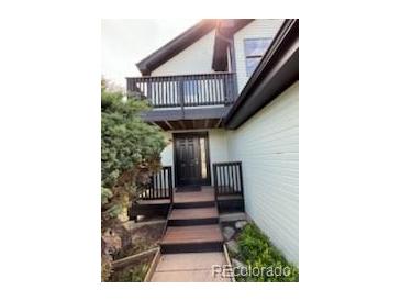 Inviting home entrance with a striking black door, complemented by a dark wood balcony, and wood stairs at 4362 Denmark Ct, Denver, CO 80239