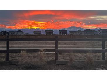 Scenic view of a colorful sunset sky over the neighborhood homes, framed by a rustic wooden fence and distant mountains at 12863 Crane River Dr, Firestone, CO 80504