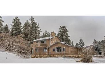 Charming log home featuring a stone chimney, balcony, and a snowy wooded setting at 11531 S Deer Creek Rd, Littleton, CO 80127