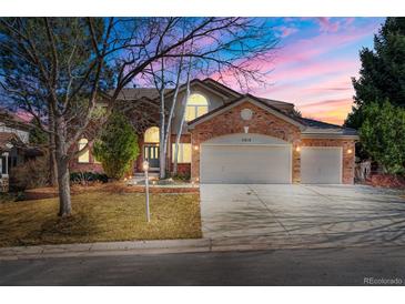 Stunning brick home featuring a 3-car garage, well-manicured lawn, and mature trees against a vibrant sunset sky at 21548 E Ottawa Cir, Aurora, CO 80016