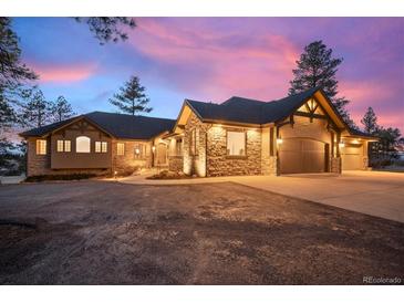 Stunning exterior view of a stone and wood home with a spacious driveway and a colorful sky at dusk at 121 County Road 146, Elizabeth, CO 80107