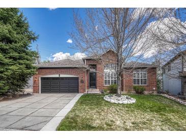 Charming brick home featuring a well-manicured lawn, dark garage door, and classic architectural details at 12344 Turquoise Terrace St, Castle Pines, CO 80108
