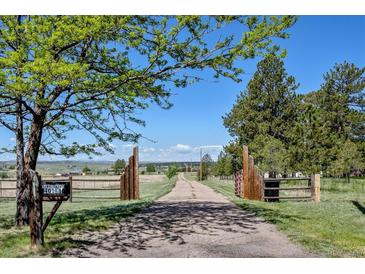 A long gravel driveway leads to a property, framed by wooden gates and lush greenery under a sunny sky at 40121 County Road 21, Elizabeth, CO 80107