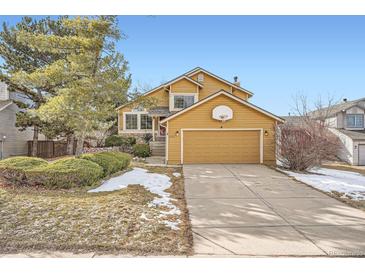 Charming mustard home featuring a two-car garage and well-maintained front yard with green grass and stone details at 9383 Cobblecrest Dr, Highlands Ranch, CO 80126