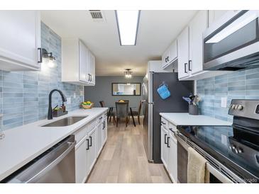 Galley kitchen with stainless appliances, light wood floors, and blue tiled backsplash at 7335 E Quincy Ave # 107, Denver, CO 80237