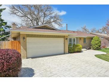 Charming brick home featuring an attached garage and a beautifully paved driveway under a sunny, blue sky at 2243 S Olive St, Denver, CO 80224