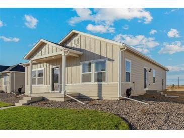 One-story home with light beige siding, a covered porch, and landscaping at 2958 Oxley St, Strasburg, CO 80136