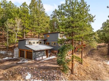 Modern home featuring gray siding, a two-car garage, and surrounded by a dense forest at 4986 White House Trl, Evergreen, CO 80439