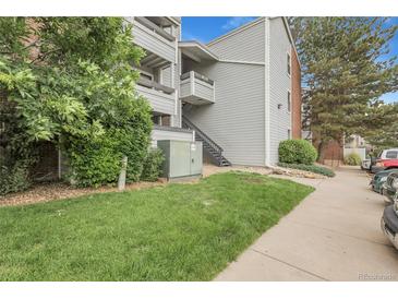 Exterior shot of a light gray condo building with well-maintained landscaping, sidewalk, and partial parking view at 14214 E 1St Dr # B08, Aurora, CO 80011