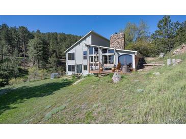 Mountain home with stone chimney, outdoor deck, mature trees, and grassy area at 100 Wildcat Ln, Boulder, CO 80304