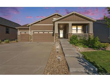 Inviting brown home with a 2-car garage, stone accents, and a welcoming front porch at dusk at 24028 E Caleb Pl, Aurora, CO 80016