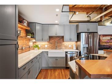Modern kitchen features gray cabinetry, stainless steel appliances, farmhouse sink, and exposed brick backsplash at 1801 Wynkoop St # 518, Denver, CO 80202