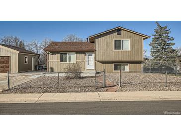 Two-story home with neutral siding, brown roof, gravel yard, and chain-link fence at 7611 Fernando Rd, Denver, CO 80221