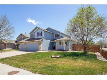 Inviting two-story blue home with stone accents, lush green lawn, and mature trees on a sunny day at 11416 E 114Th Ave, Commerce City, CO 80640
