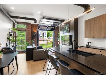 Modern living room featuring hardwood floors, exposed brick, and a glass garage door opening to the outside at 1242 Yates St # U2, Denver, CO 80204