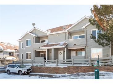 View of gray two story townhome exterior with patios, brick accents, and a gray fence in a snowy landscape at 912 S Yampa St # 206, Aurora, CO 80017