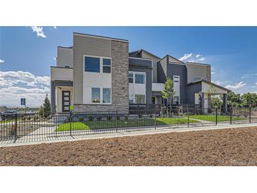 Modern townhome featuring stone accents, neutral siding, landscaped front yard, and metal perimeter fencing at 6880 Bryant Way, Denver, CO 80221