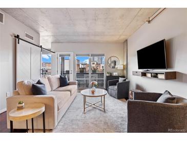 Bright living room with a barn door, hardwood floors, a comfortable sofa and a balcony with city views at 1475 Delgany St # 306, Denver, CO 80202