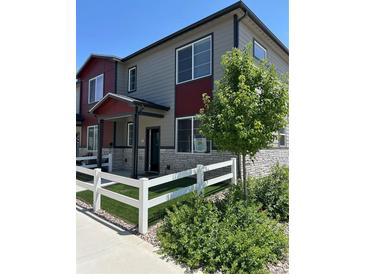 Charming townhome featuring gray siding, a red accent wall, and a welcoming white picket fence at 1353 Reynolds St # 5A, Fort Lupton, CO 80621