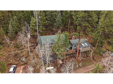 A charming home nestled in a wooded area, with a green roof and a lovely deck at 7510 Blue Creek Rd, Evergreen, CO 80439