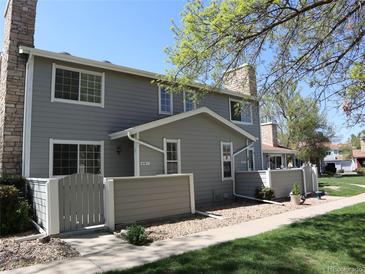 Two-story townhome with gray siding, stone chimney, and a well-maintained front yard under a clear blue sky at 8418 Everett Way # C, Arvada, CO 80005