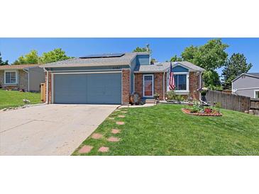 Charming single-story home with an attached garage, red brick accents, and lush green lawn at 6085 S Parfet St, Littleton, CO 80127