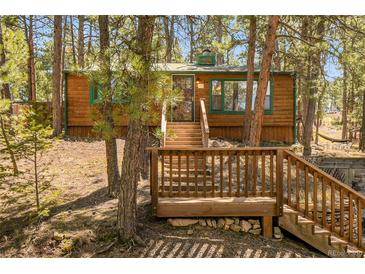 Exterior view of a wooden cabin surrounded by trees, featuring a deck and staircase, perfect mountain living at 5235 Cheyenne Rd, Indian Hills, CO 80454