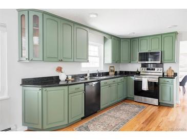 Charming kitchen featuring green cabinets, black countertops, stainless steel appliances, and hardwood floors at 6982 Estes Dr, Arvada, CO 80004
