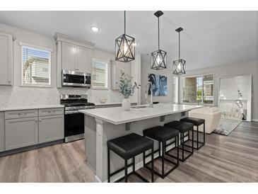 Stylish kitchen featuring gray cabinetry, stainless steel appliances, and a large island with modern pendant lighting at 16421 Askins Loop, Parker, CO 80134