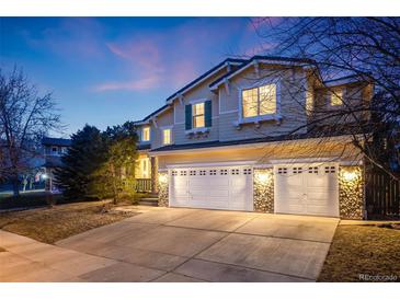 Stunning two-story home with a three-car garage and stone accents, illuminated by warm exterior lighting at dusk at 683 Ridgemont Cir, Highlands Ranch, CO 80126