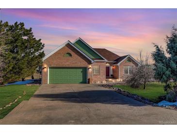 Beautiful brick home with an attached green garage and a well-manicured lawn at dusk at 4270 Defoe St, Strasburg, CO 80136