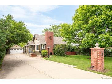Charming exterior features a well-maintained lawn, a brick chimney, and a detached two car garage with a long driveway at 3317 Harlan St, Wheat Ridge, CO 80033