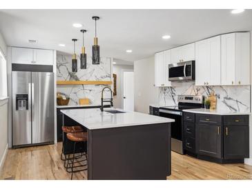 Modern kitchen with stainless steel appliances, a large island with marble backsplash, and custom lighting fixtures at 7320 W 21St Ave, Lakewood, CO 80214