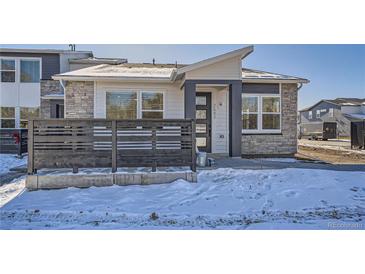 Charming modern home with stone accents, gray trim, and a small fenced yard with snow at 2507 W 69Th Pl, Denver, CO 80221
