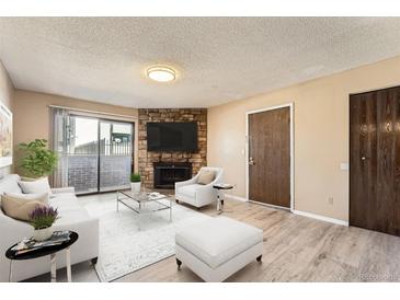Cozy living room featuring a stone fireplace, light wood floors, and sliding door to the balcony at 11937 E Harvard Ave # 102, Aurora, CO 80014
