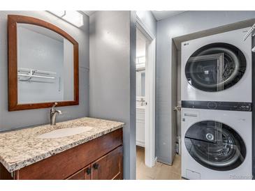 Bathroom vanity with granite countertop, wooden cabinets and a stacked washer and dryer unit at 2929 W Floyd Ave # 217, Denver, CO 80236