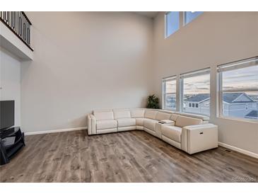 Bright living room with a large sectional sofa, wood floors, and soaring ceilings with many windows allowing ample natural light at 17203 Birds Foot Ave, Parker, CO 80134