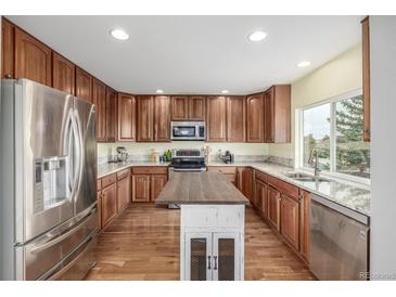 Well-lit kitchen features stainless steel appliances, wood cabinets, granite counters, island and hardwood floors at 16523 High Desert Pl, Parker, CO 80134