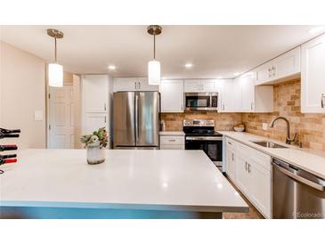 Bright kitchen features stainless appliances, tile backsplash, white cabinets, and center island with quartz countertop at 13961 E Marina Dr # 414, Aurora, CO 80014